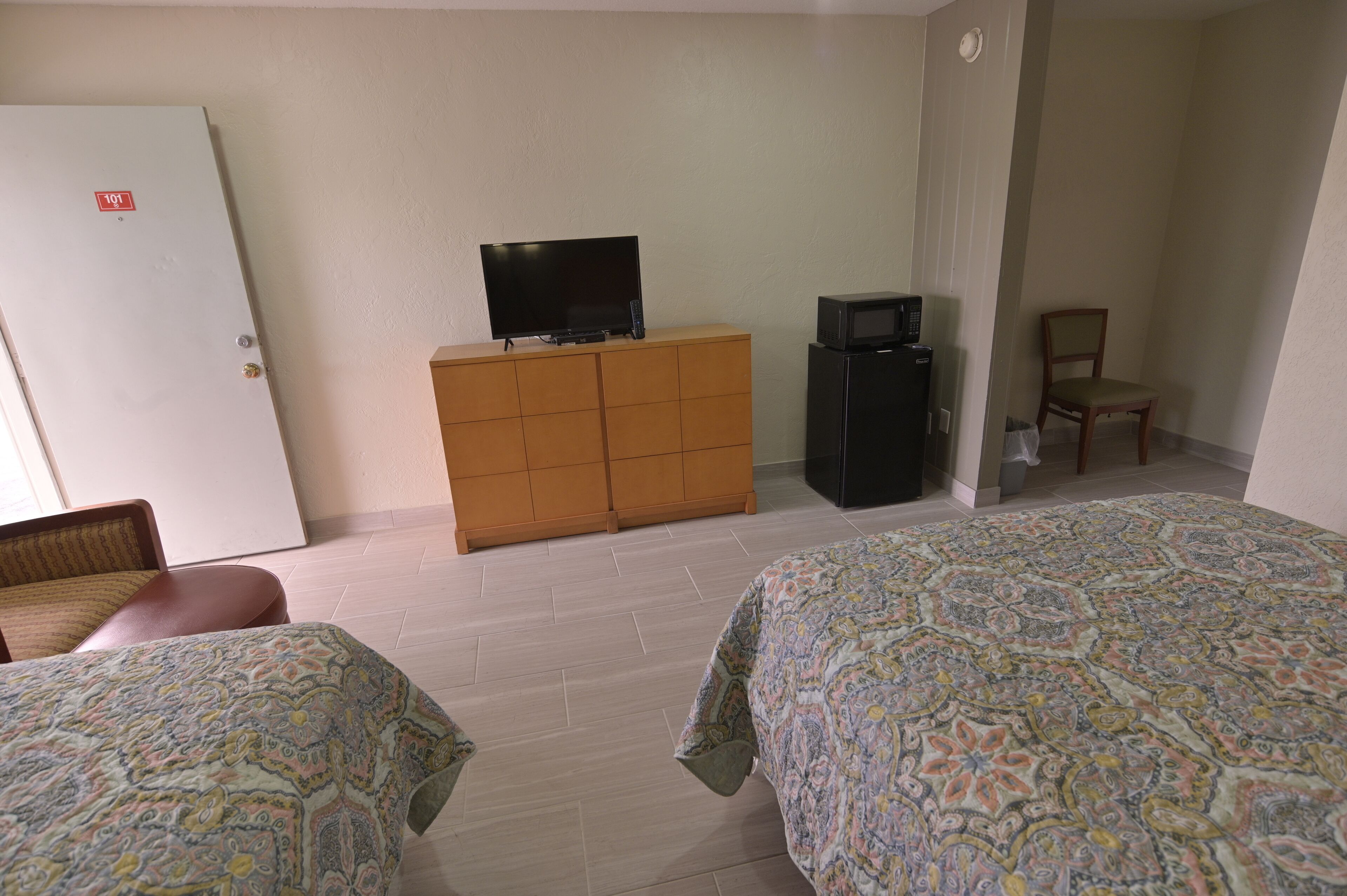 Una habitación de hotel con dos camas, un televisor sobre un aparador de madera, un microondas y una silla.