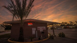 A brick motel office with a neon sign, a palm tree, and a 'No Parking' sign. - Deluxe Inn (Bunnell)