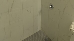 A bathroom with white marble tiles, a shower with a handheld showerhead, and a toilet. - Deluxe Inn (Bunnell)
