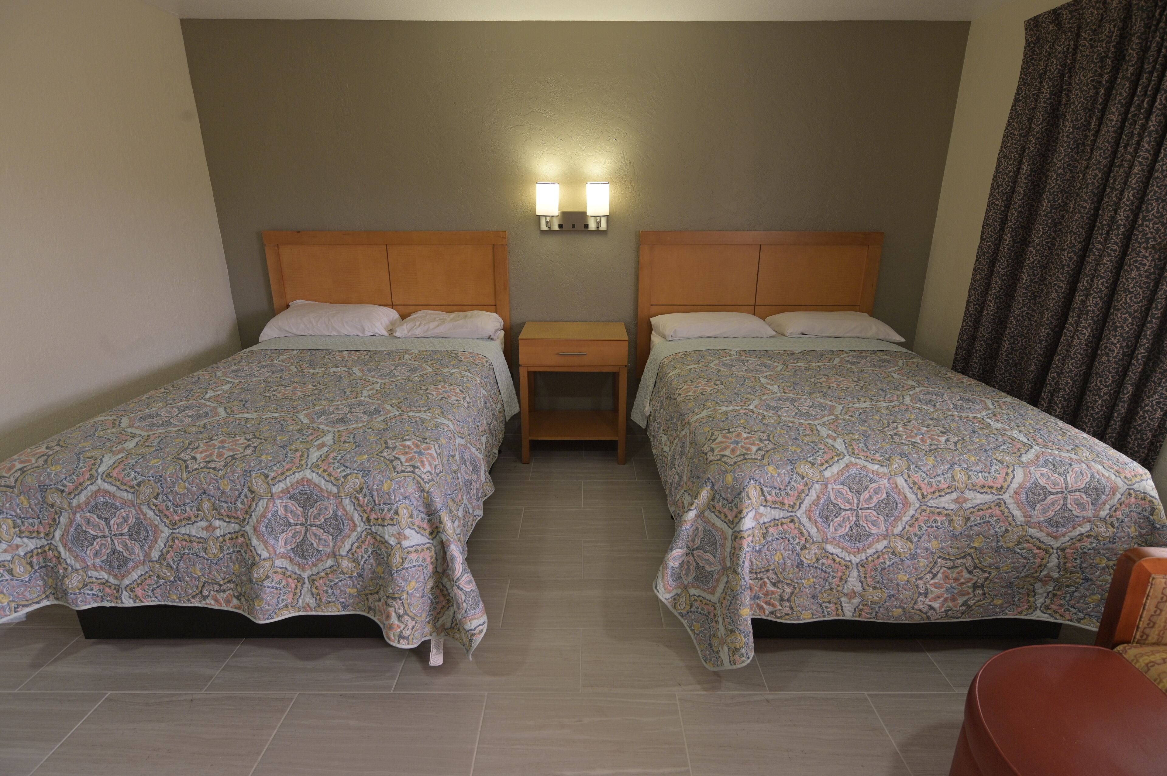 A hotel room with two beds, a nightstand, and a chair.
