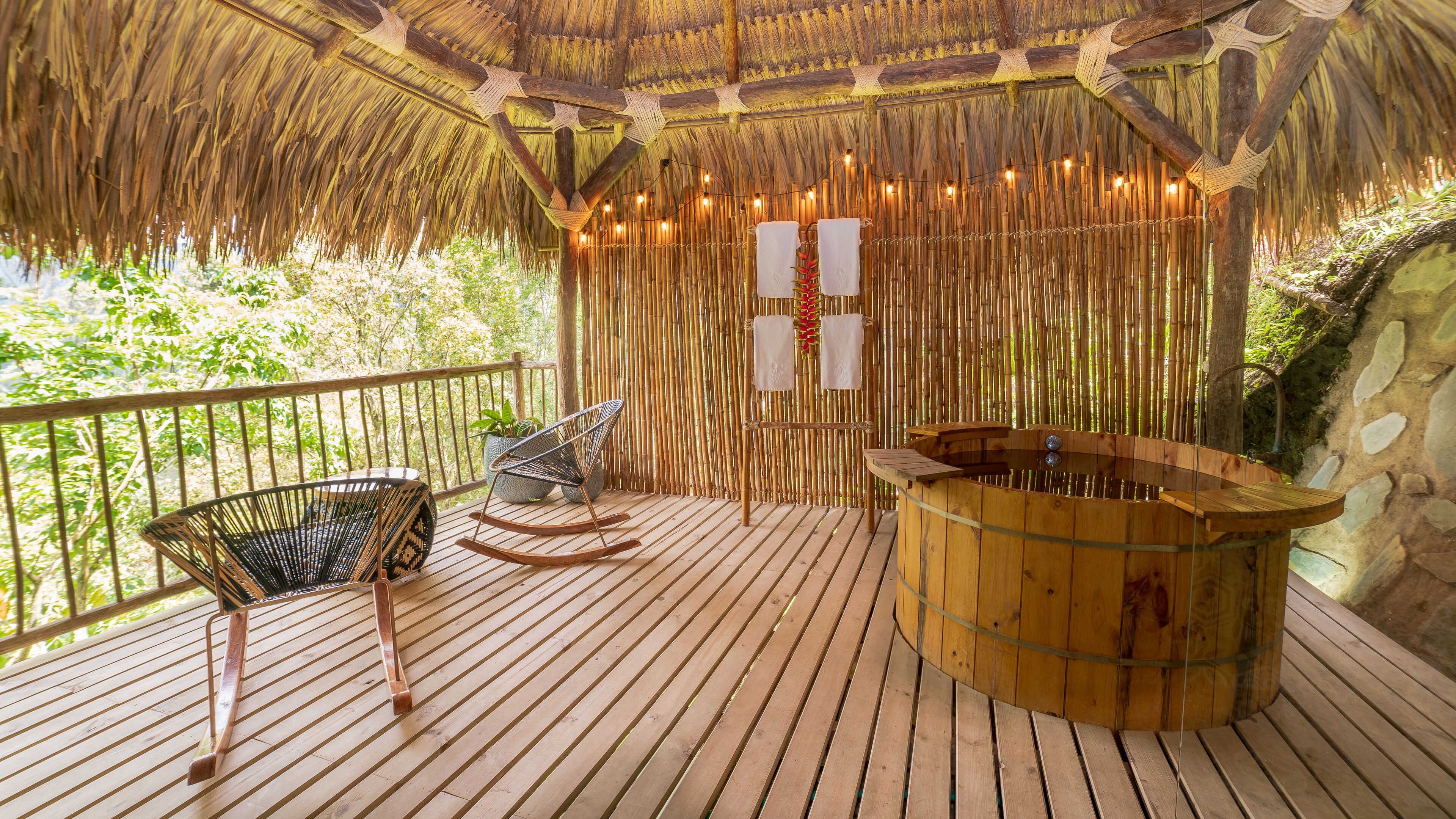 Una terraza de madera con techo de paja, un jacuzzi y dos mecedoras.