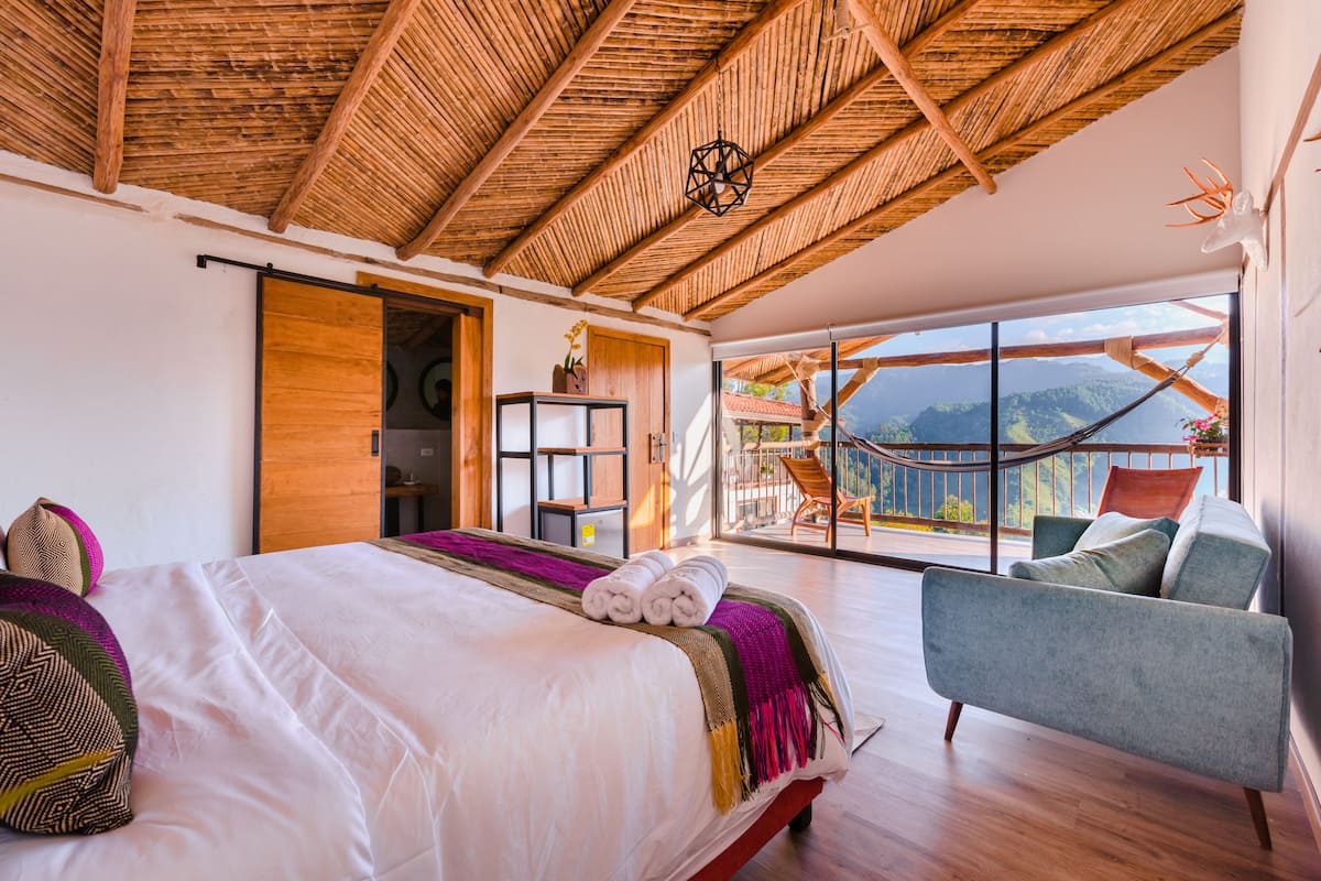 Une chambre spacieuse avec un grand lit, une vue sur les montagnes depuis un balcon et un hamac à l’extérieur.