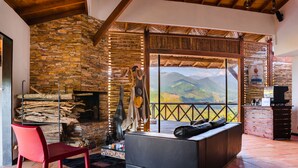 Una habitación acogedora con pared de piedra, chimenea, sillón rojo, sofá gris y vistas a la montaña.