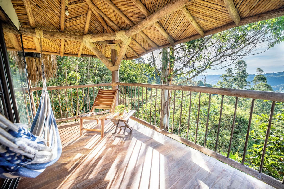 Une terrasse en bois surmontée d’un toit de chaume, deux chaises en bois et un hamac.
