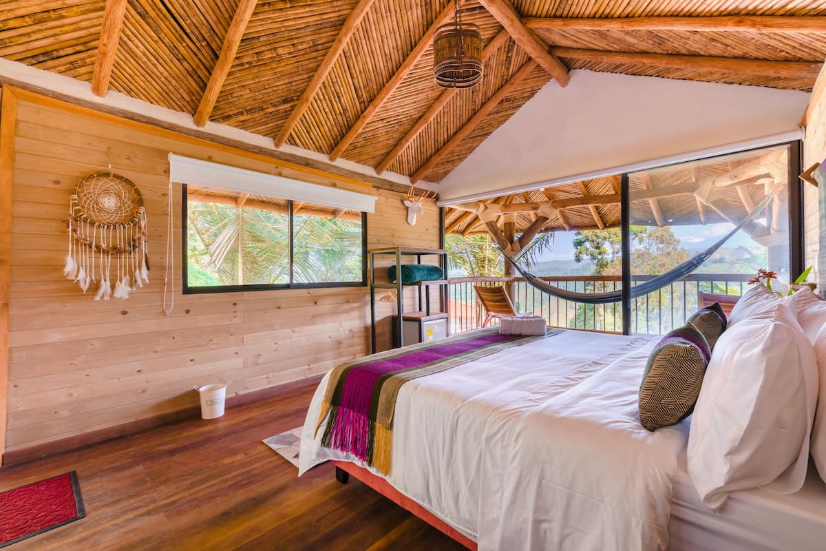 Une chambre spacieuse avec un grand lit, des murs en bois, un toit de chaume et un hamac.