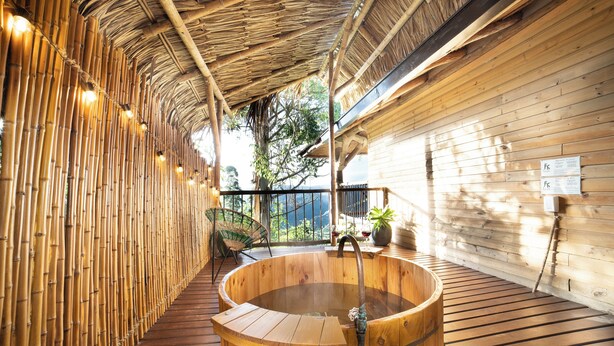 Un área de spa de madera con un jacuzzi, paredes de bambú y una terraza de madera.