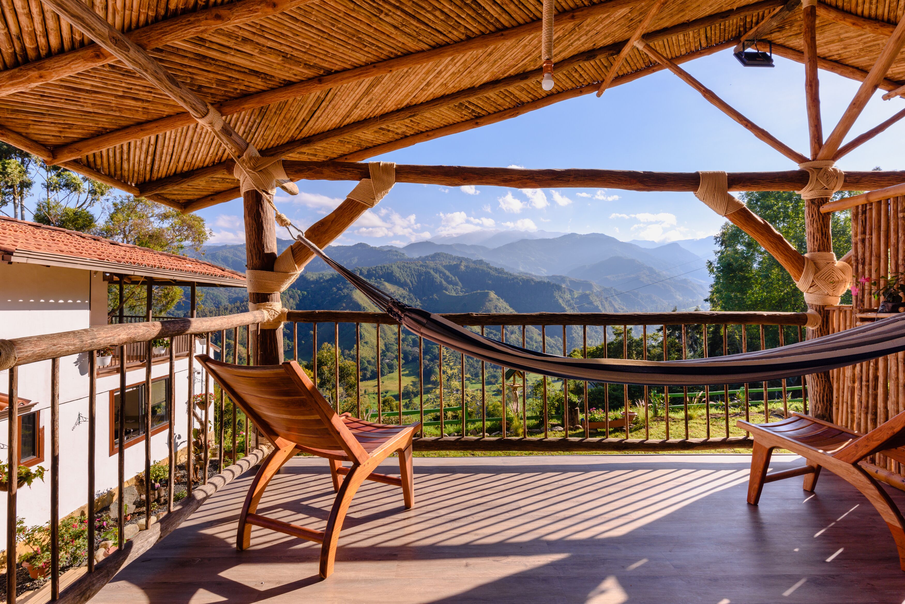 Une terrasse en bois avec un hamac, des chaises en bois et une vue sur les montagnes.