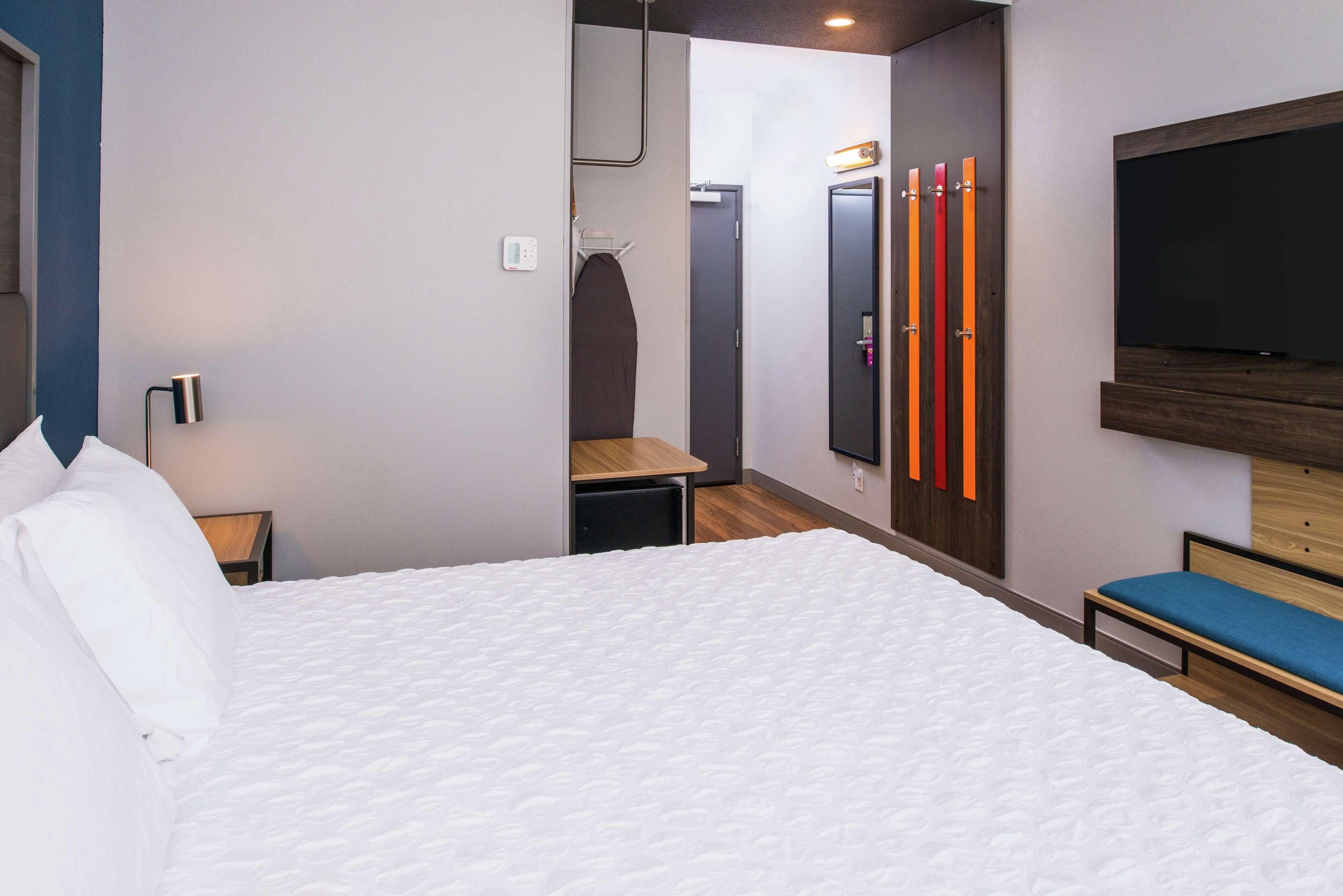 Una habitación de hotel moderna con una cama grande, un televisor en la pared y un banco.