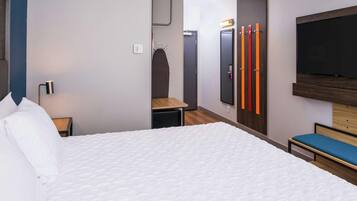 Una habitación de hotel moderna con una cama grande, un televisor en la pared y un banco.