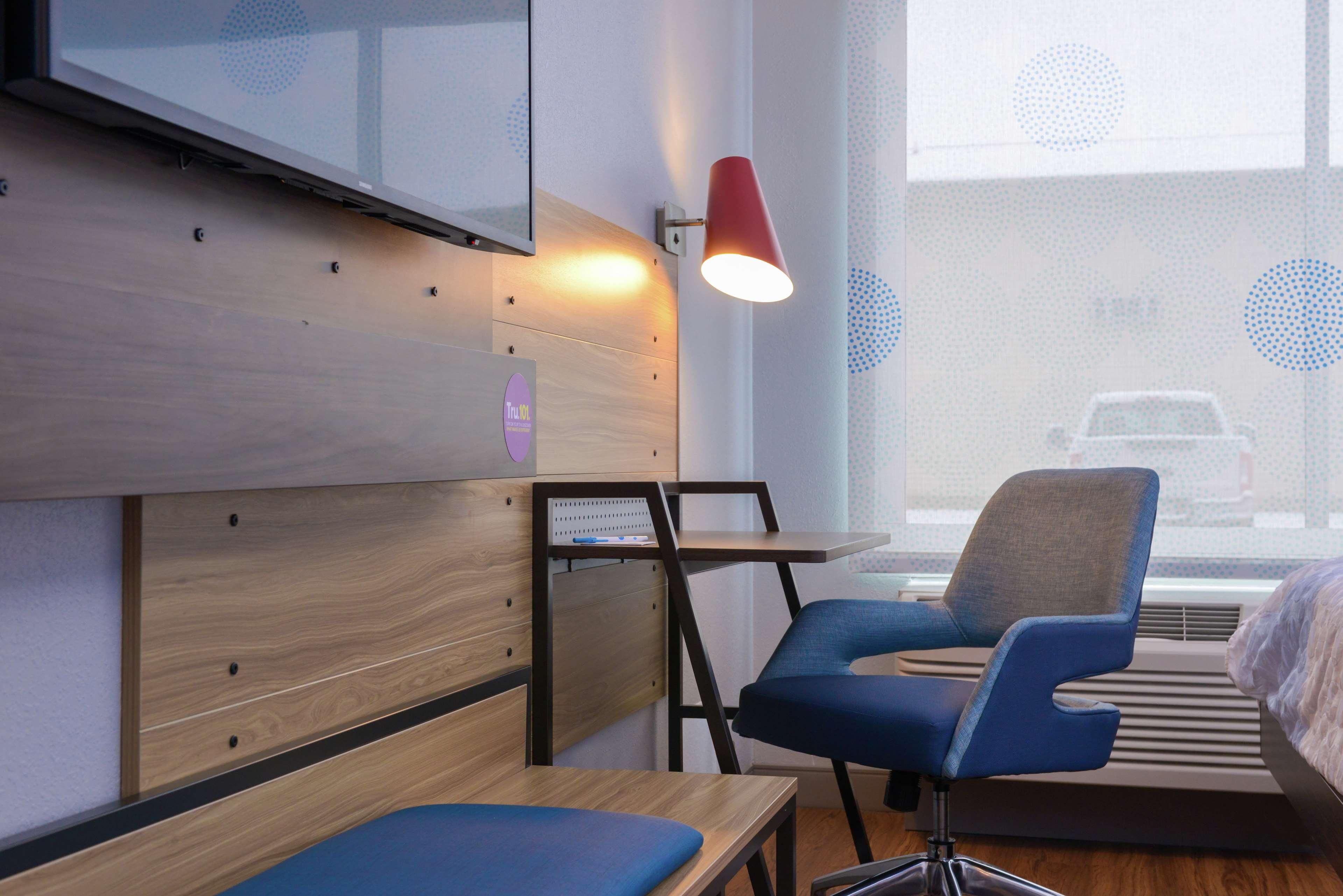 A modern hotel room with a wooden wall unit, a blue chair, a small table, and a red lamp.