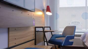 A modern hotel room with a wooden wall unit, a blue chair, a small table, and a red lamp.