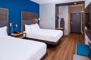 A hotel room with two beds, wooden flooring, a blue accent wall, a small desk with a lamp, and a bathroom visible through an open door. - Tru By Hilton Elkhart (Elkhart)