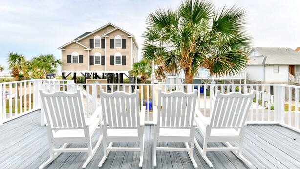 A wooden deck with white chairs and a view of a two-story building with a balcony. - 5 Bedroom Oceanview House with a Private Pool! Stingray (Surfside Beach)