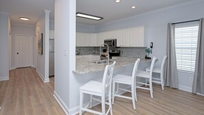 A modern kitchen with white cabinets, a granite countertop, and a built-in oven. There are three white chairs around the island. - 5 Bedroom Oceanview House with a Private Pool! Stingray (Surfside Beach)