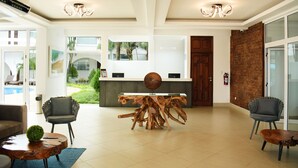 A spacious lobby with a wooden coffee table, two chairs, a reception desk, and a view of a swimming pool. - Gran Costa Azul Hotel (Puerto Barrios)