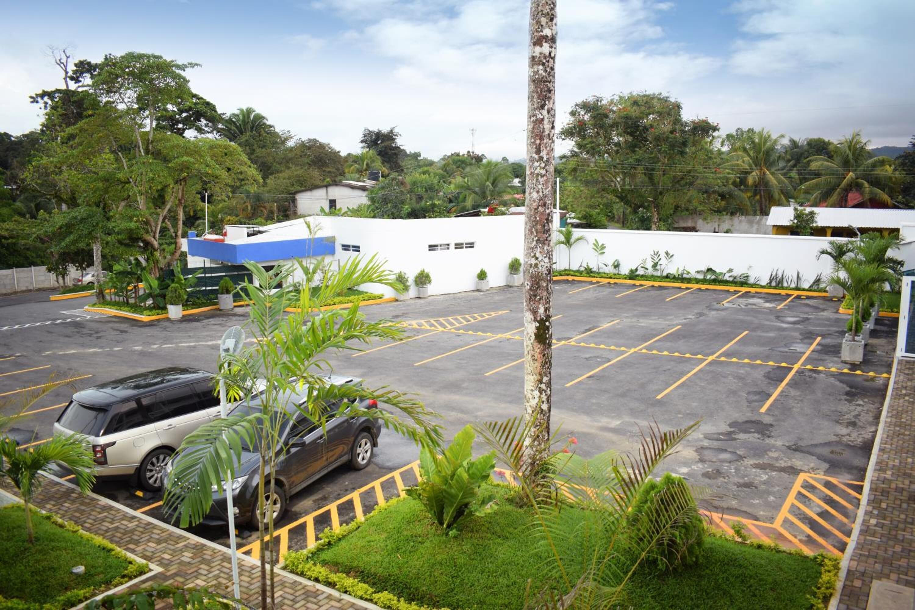 A parking area with marked spaces, a white building with a blue roof, and surrounding greenery.