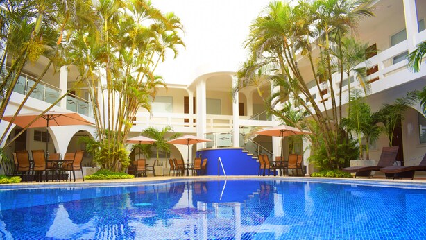 A swimming pool with lounge chairs and umbrellas, surrounded by palm trees and a multi-level building. - Gran Costa Azul Hotel (Puerto Barrios)
