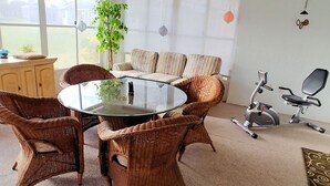 Ein Zimmer mit Korbmöbeln, einem Glastisch, einer Couch und einem Heimtrainer.