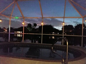 An outdoor swimming pool with a glass enclosure, surrounded by trees and a view of a distant cityscape. - Craig House Bradenton with Heated Pool - No Cleaning Fee (Bradenton)