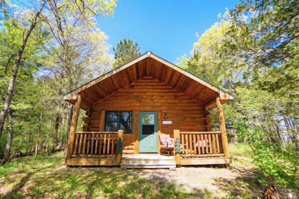 Situated in a forested area, this cabin features a cozy porch with a bench and a door with windows.