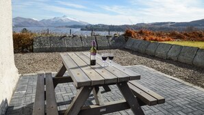 An outdoor picnic table with a bottle and glasses, set against a backdrop of mountains and a lake. - Tigh Grianach -  a cottage that sleeps 6 guests  in 3 bedrooms (Oban)