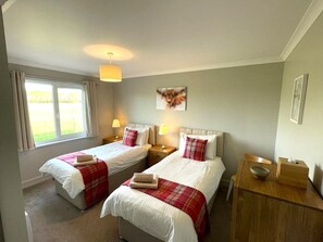 A hotel room with two beds, a window, a painting, and a bedside table.