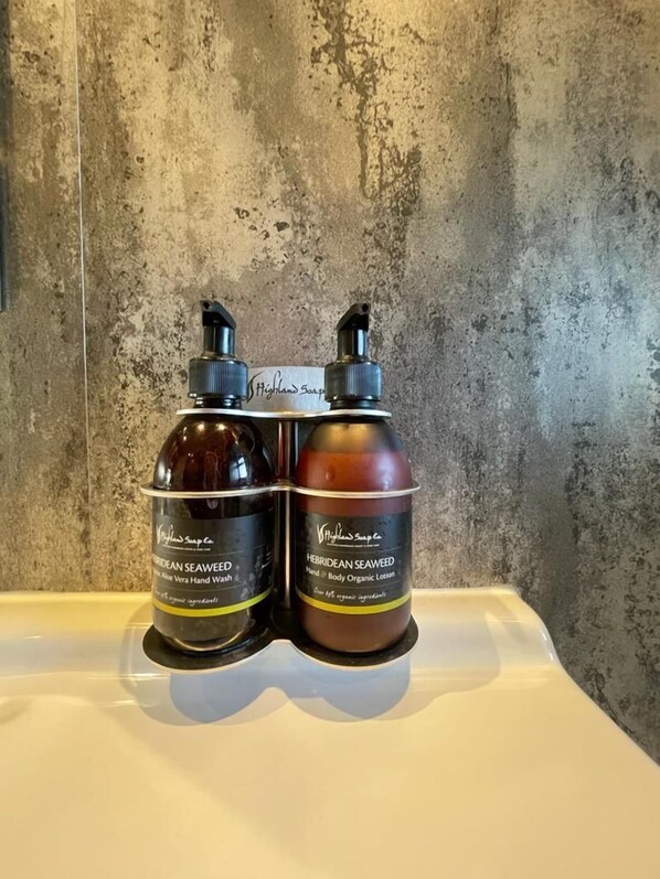 Deux bouteilles de savon Highland sont posées sur une surface blanche, devant un mur à texture.