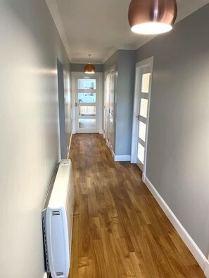 Un couloir doté d’un plancher en bois, de murs blancs et d’un luminaire au plafond.