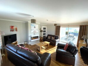 A modern living room with a flat-screen TV, leather sofas, a wooden coffee table, and a fireplace.