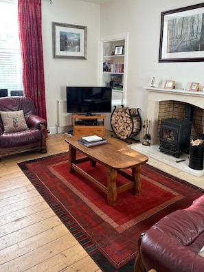 Una sala de estar con un sofá de cuero, una mesa de centro de madera, un televisor de pantalla plana, una chimenea y una estantería.
