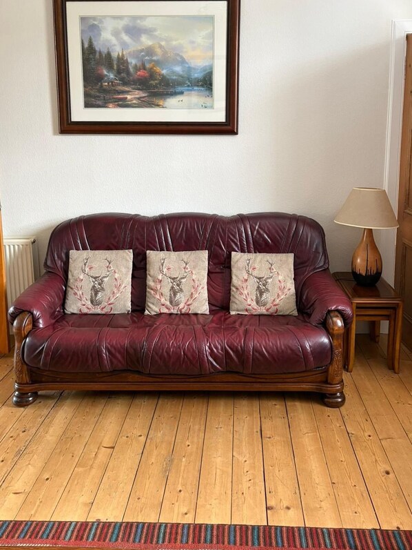 A leather sofa with floral cushions, a framed landscape painting, a wooden floor, and a lamp.