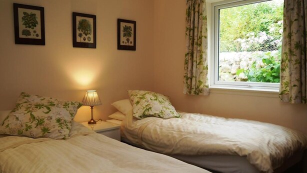 A bedroom with two single beds, a bedside table with a lamp, and a window with curtains. - Seabank Cottage -  a cottage that sleeps 6 guests  in 3 bedrooms (Dalbeattie)