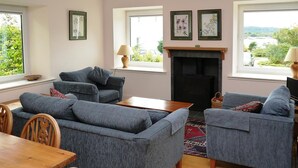 A living room with a fireplace, two sofas, a dining table, and chairs. - Seabank Cottage -  a cottage that sleeps 6 guests  in 3 bedrooms (Dalbeattie)