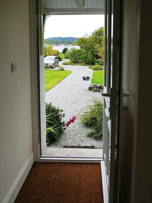 A doorway leading to a gravel driveway with a car parked on the side.