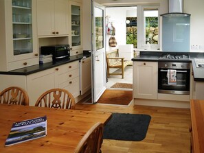 Une cuisine compacte avec des meubles blancs, un plan de travail noir et un coin repas comprenant une table et des chaises en bois.