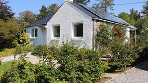 A white house with a sloped roof, a chimney, and solar panels. - Seabank Cottage -  a cottage that sleeps 6 guests  in 3 bedrooms (Dalbeattie)