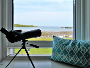 Ein Teleskop auf einem Stativ vor einem Fenster mit Blick auf einen Strand.