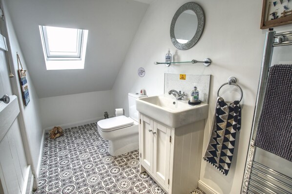A bathroom with a white toilet, a sink with a mirror above, patterned floor tiles, and a towel rack with a patterned towel.
