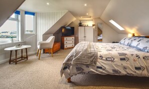 A bedroom with a bed, a chair, a TV, a dresser, and a window with a view.