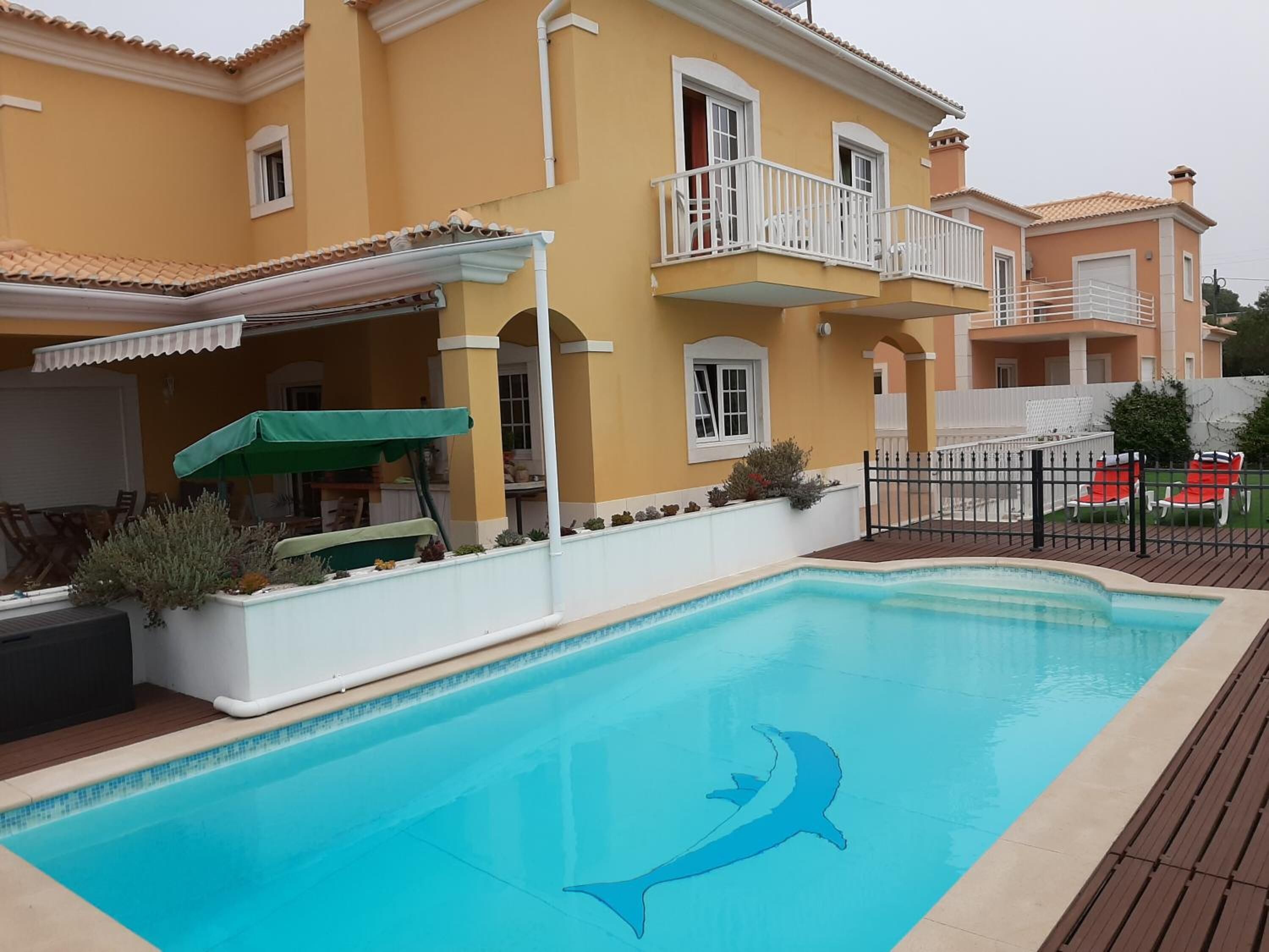 Ein Schwimmbecken mit Delphin-Motiv, eine überdachte Terrasse und ein umzäunter Außenbereich mit Sitzgelegenheiten.