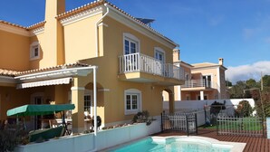 Un edificio de dos pisos con piscina, un patio cubierto y un jardín cercado.