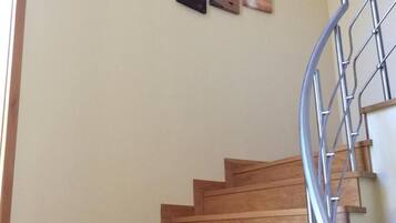 A wooden staircase with a metal handrail, leading to a landing where three framed artworks are displayed on the wall.