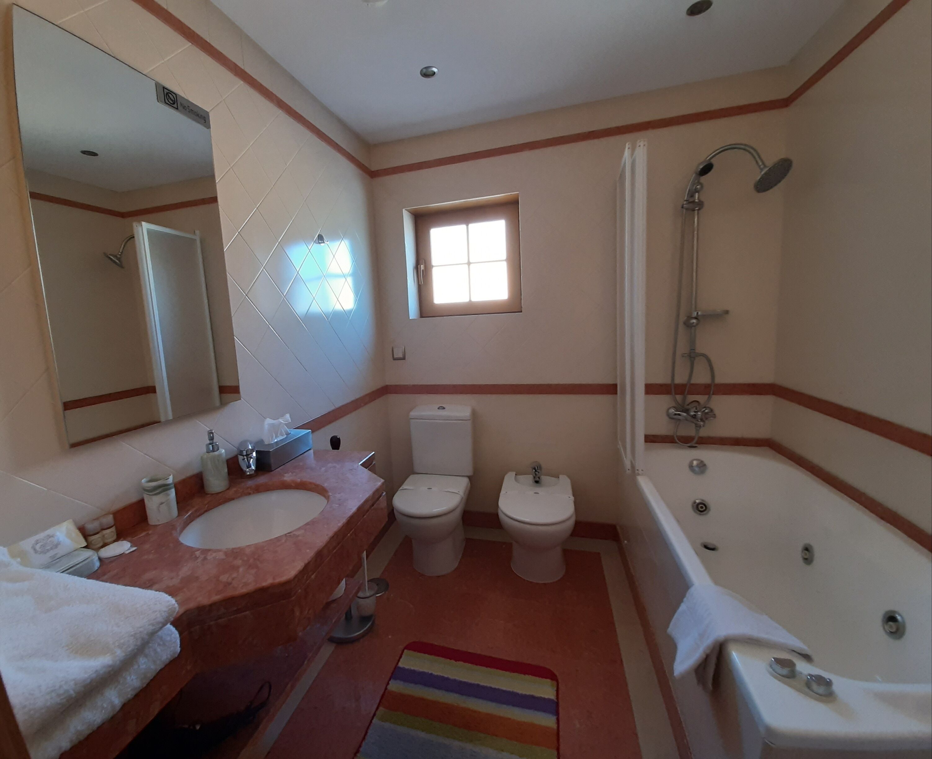 A bathroom with a double sink, a toilet, a bathtub, and a window.