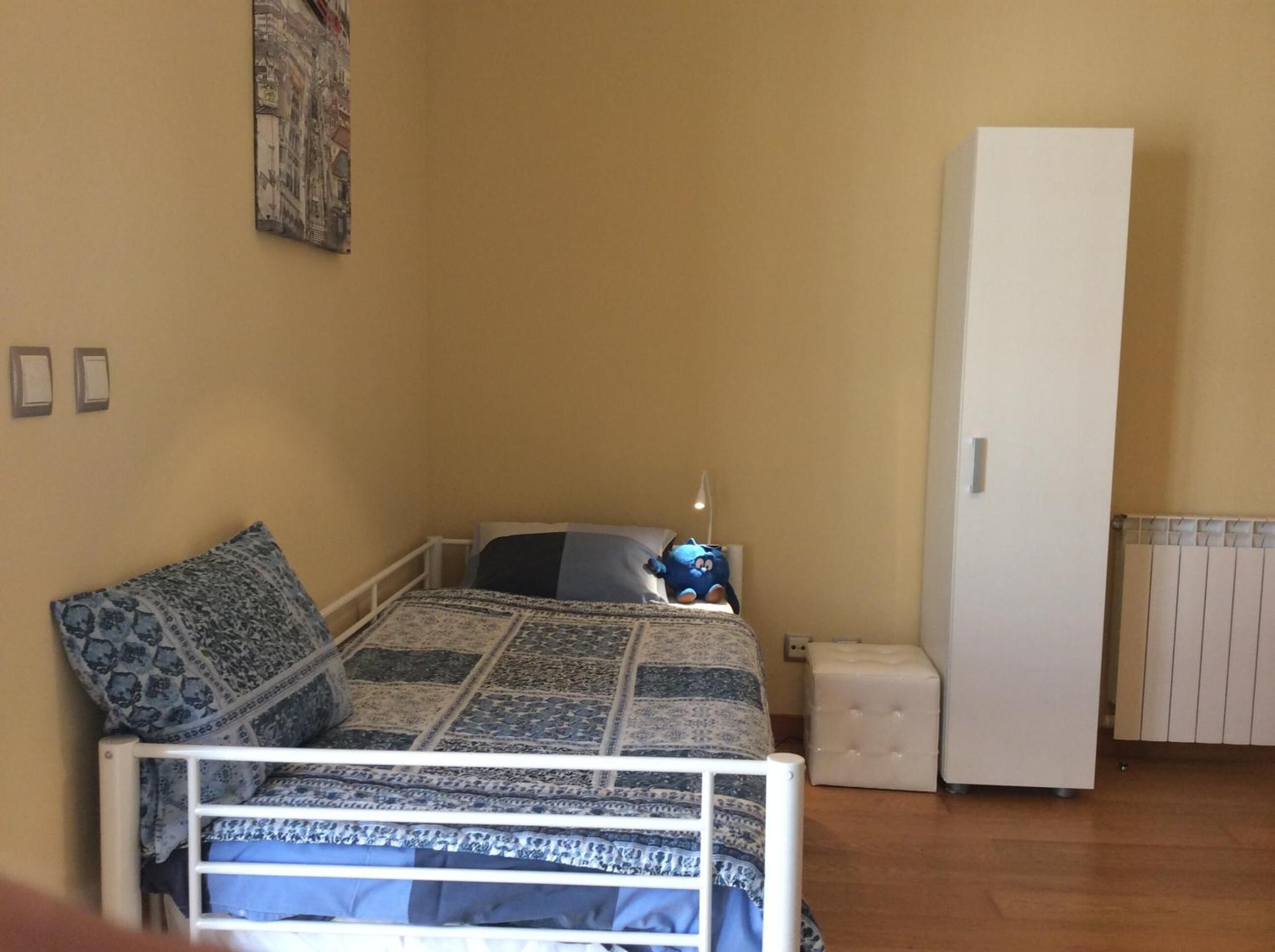 Ein kleines Zimmer mit einem Einzelbett, einer gestreiften Bettdecke, einem weißen Kleiderschrank und einem Heizkörper.