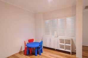 Ein Zimmer mit einem runden Tisch, Stühlen, einem Heizkörper und einem Fenster mit Fensterläden.