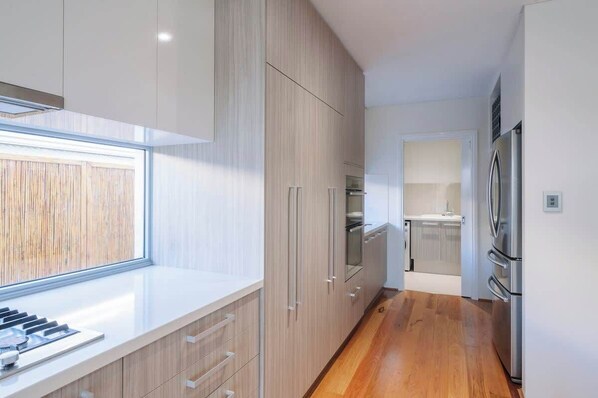 Eine moderne Küche mit Holzschränken, einem Edelstahlkühlschrank und einem Fenster für natürliches Licht.