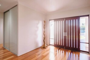 A modern room with a sliding glass door, a wooden floor, and a sculptural piece. - Ceol Na Mara—Luxury Pool Escape with Golf Views (Dunsborough)