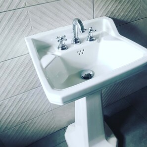 Un lavamanos pedestal blanco con dos grifos y un solo orificio de desagüe.