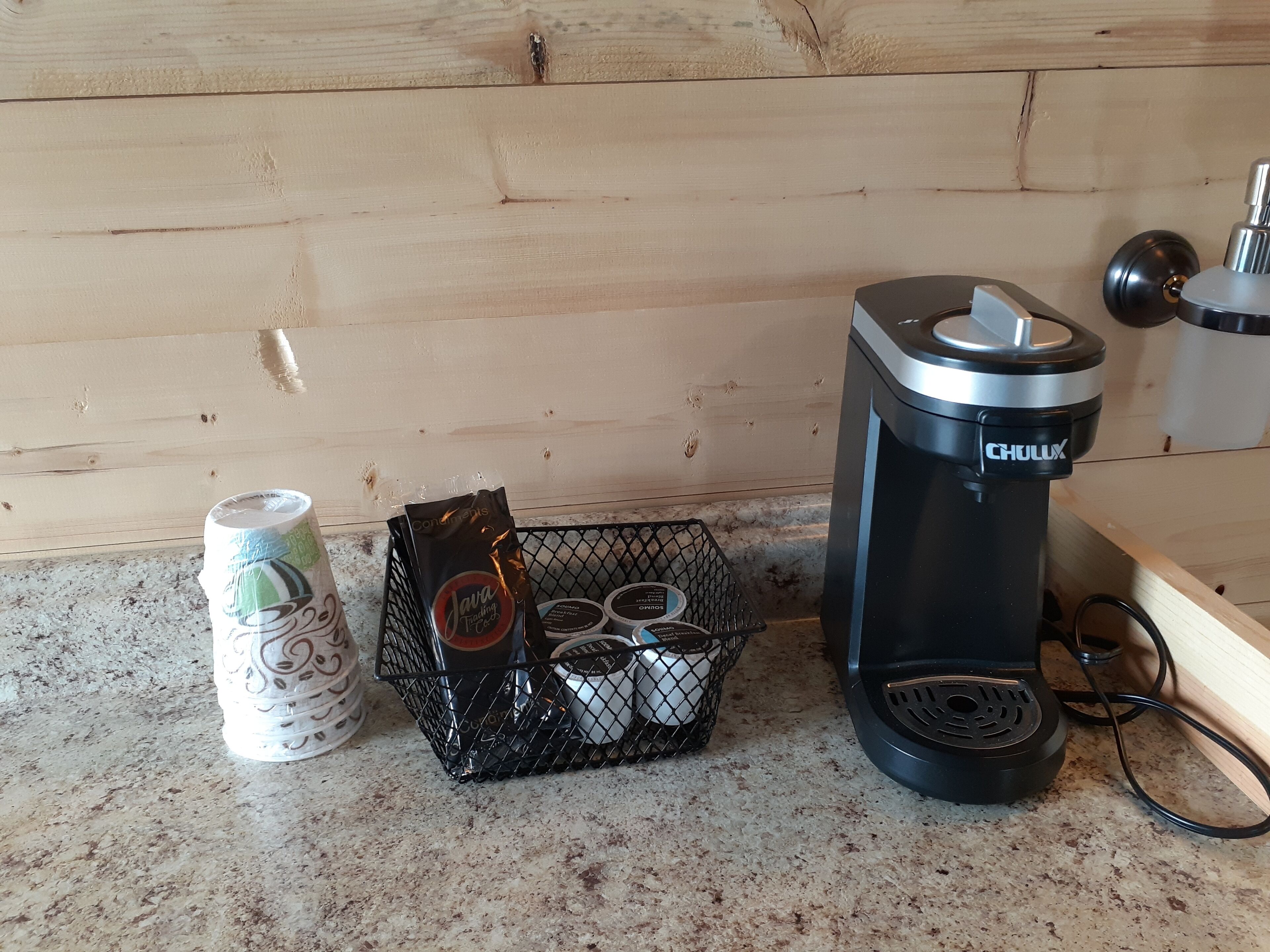 A kitchen counter with a coffee maker, a can of soda, and a basket containing coffee pods.