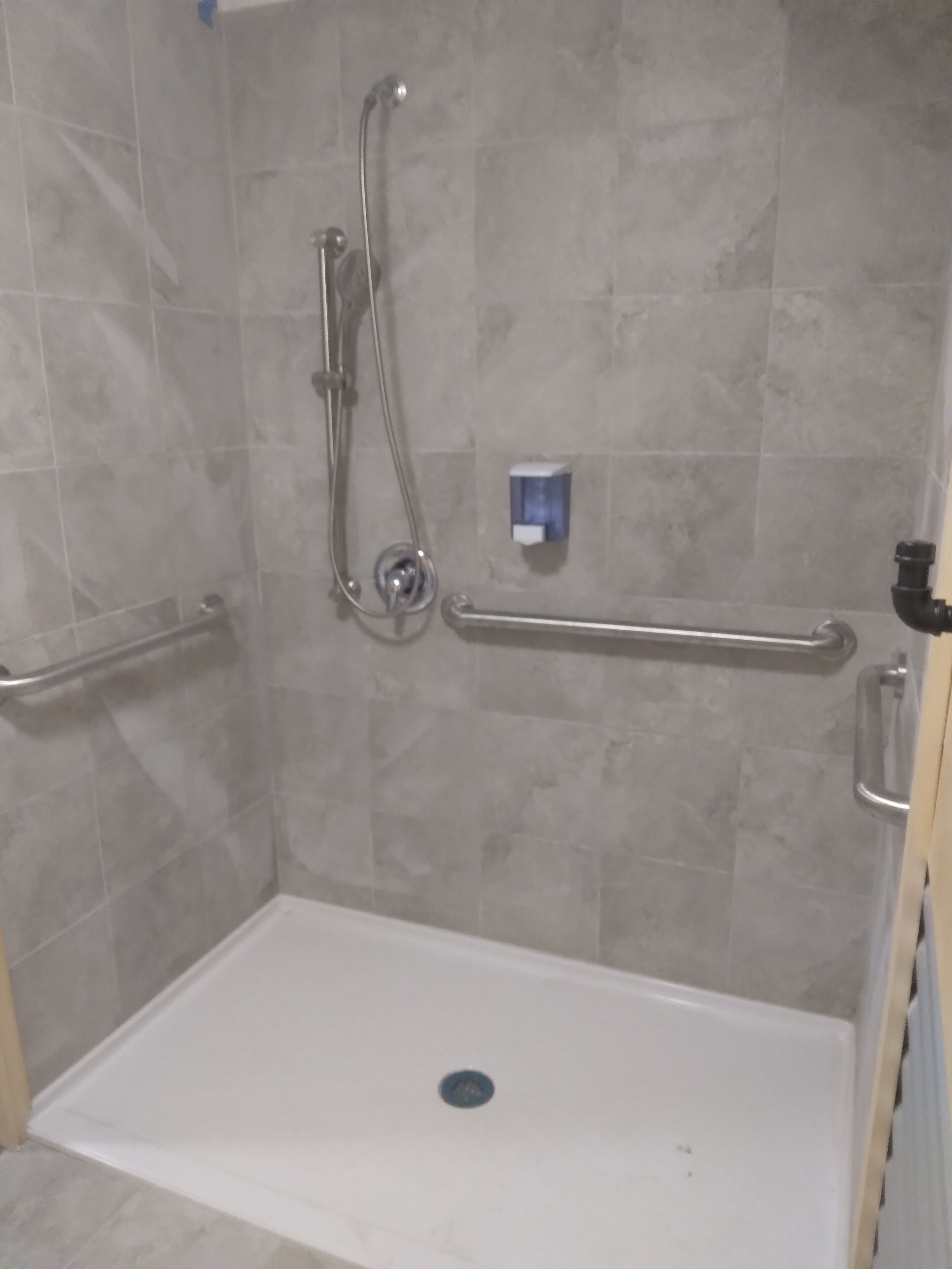 A shower area with a white floor, a handheld showerhead, a wall-mounted faucet, and a handrail.
